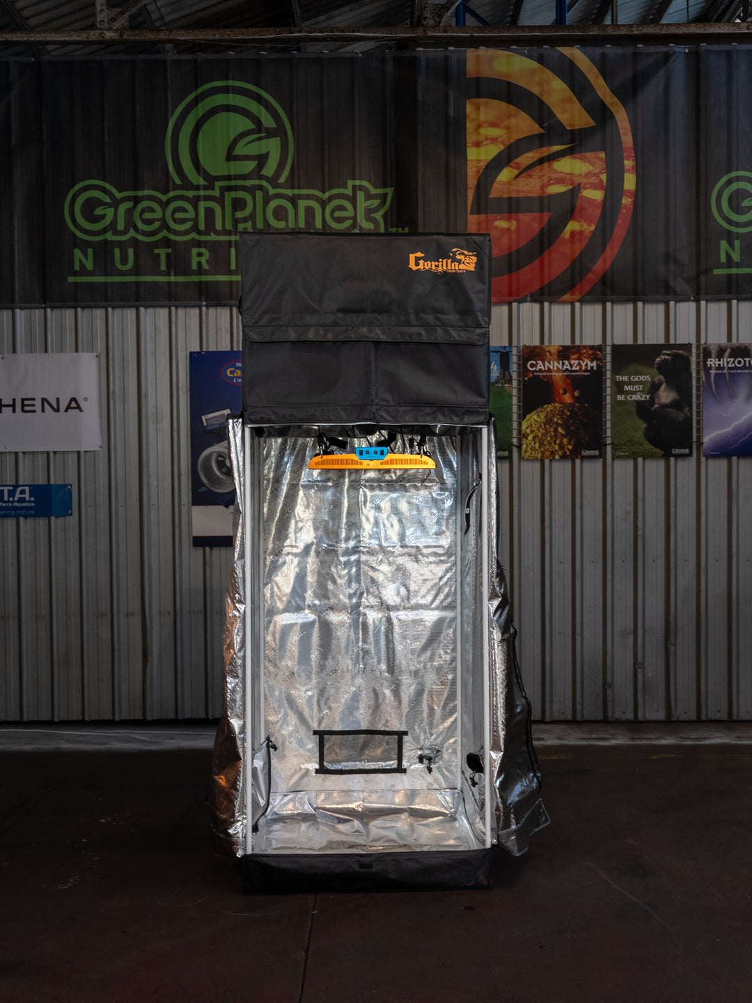 Silver grow tent with 'Green Planet' branding against a backdrop of various posters and banners.