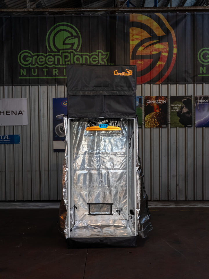 Silver grow tent with 'Green Planet' branding against a backdrop of various posters and banners.
