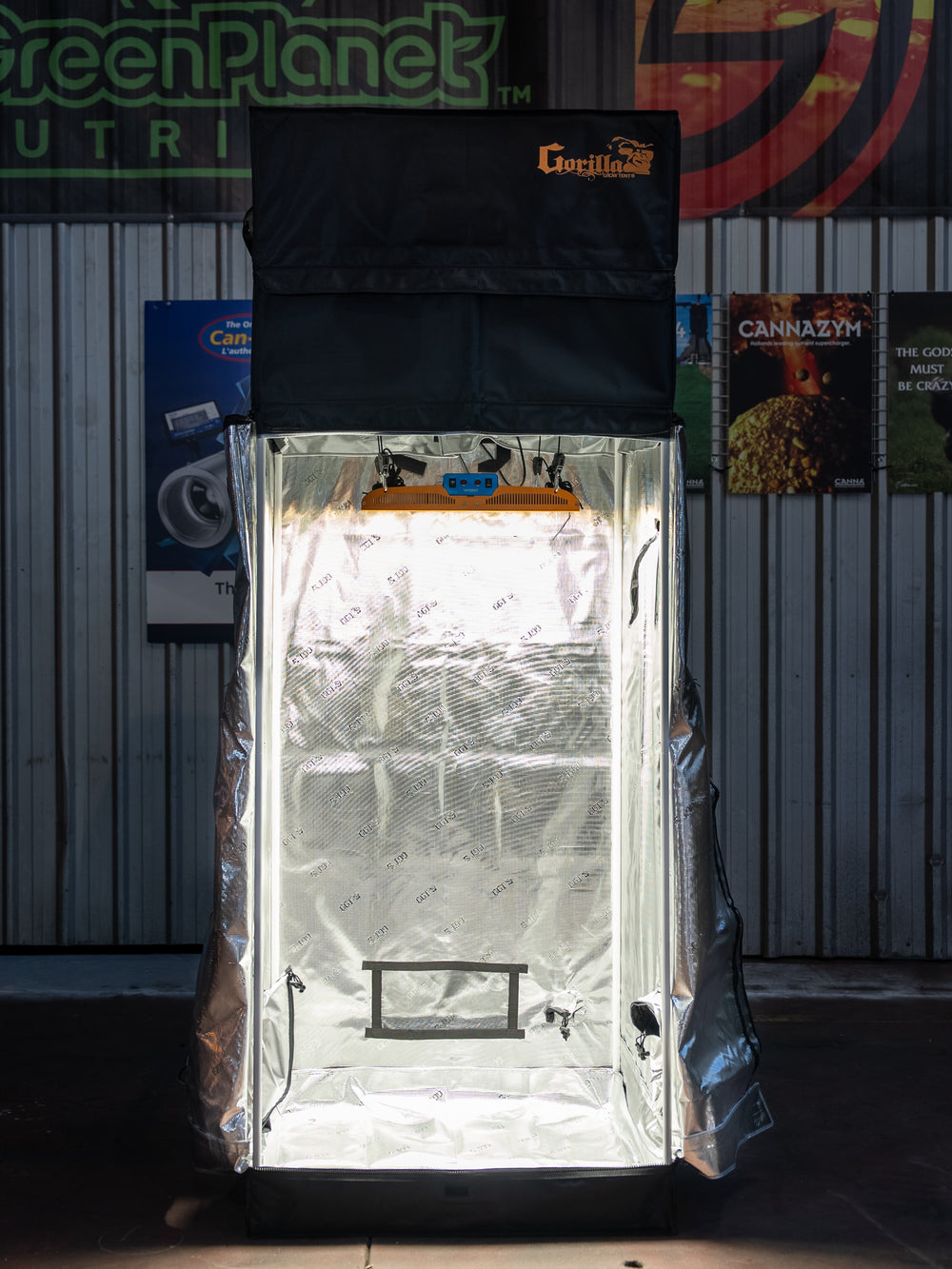 Greenhouse with a light on inside, branded 'Cannalite', against a wall with various posters.